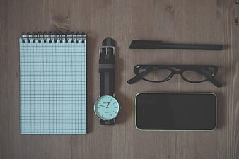 Flat lay of notebook, watch, glasses, and smartphone on wood
