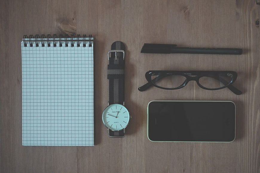 Flat lay of notebook, watch, glasses, and smartphone on wood
