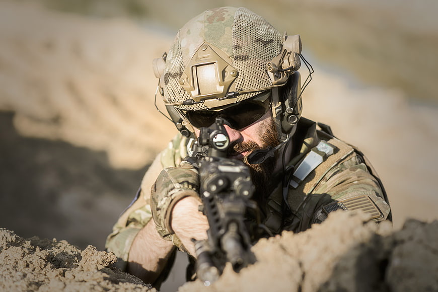 Soldier aiming rifle from sand trench in desert