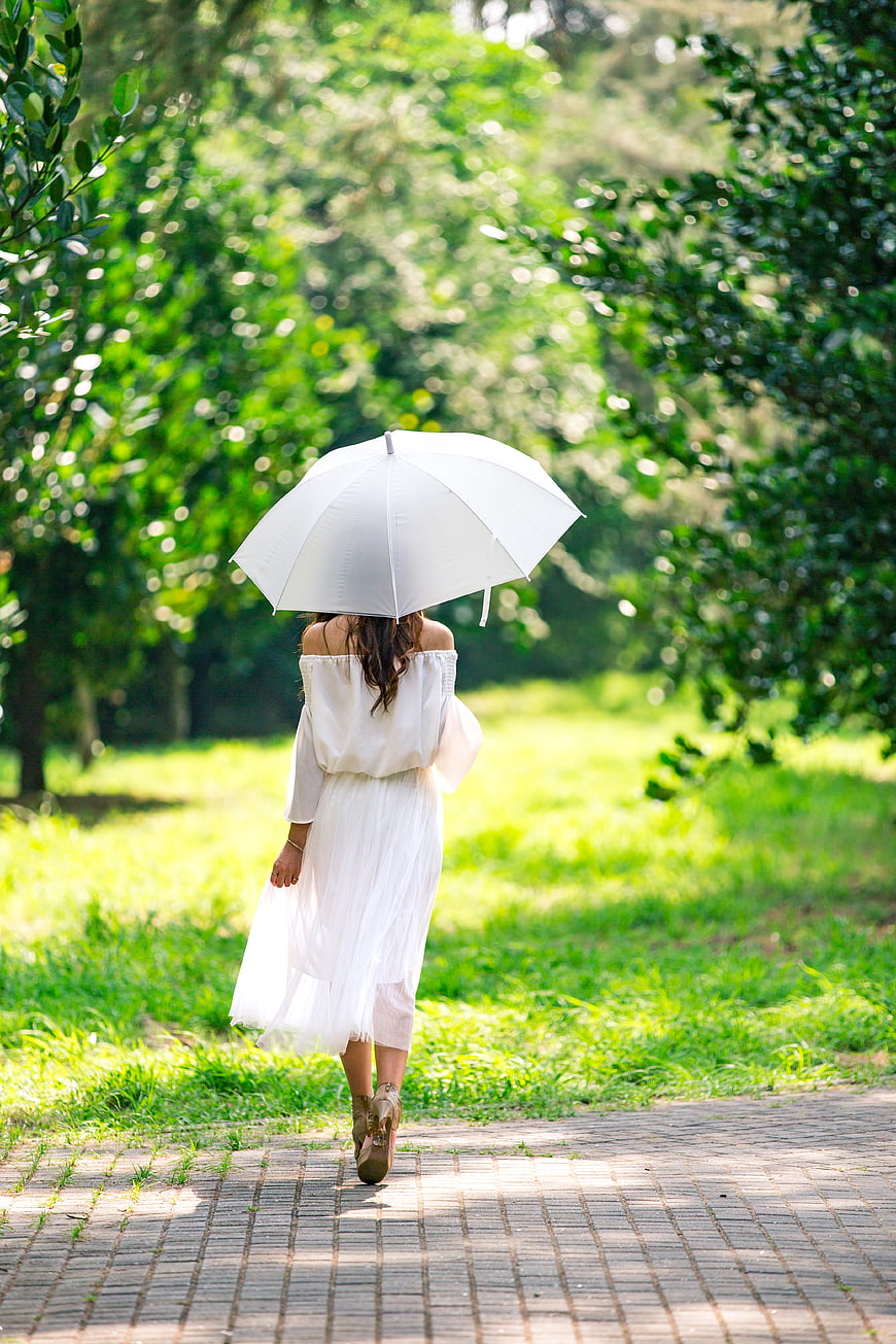Woman in White Dress Walking with Umbrella in Park