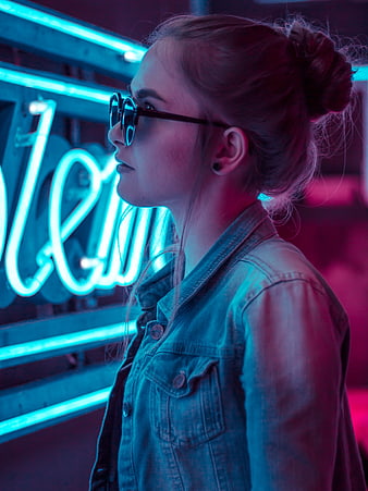 Young woman in denim jacket and sunglasses against neon lights