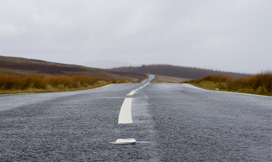 Wet asphalt road stretching into misty hills on an overcast day