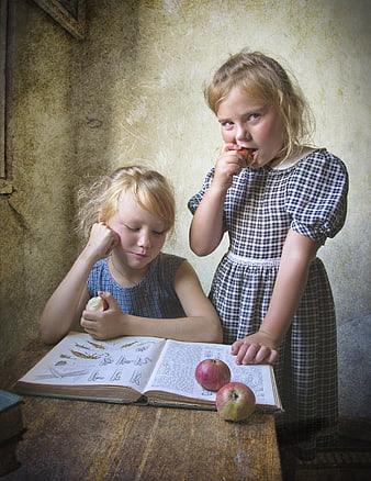 Two young girls reading an old book and eating apples