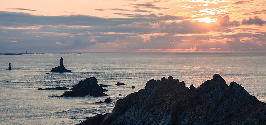 Dramatic Sunset Over Rocky Coastline with Lighthouse Silhouette