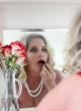Blonde woman applying lipstick in mirror with roses