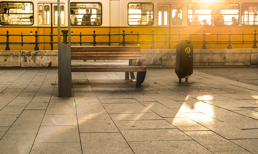 Sunlit yellow tram at urban station with empty bench