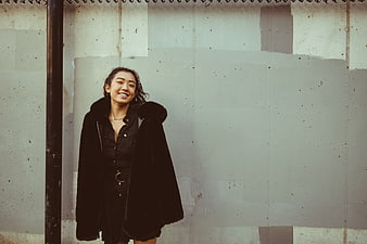 Happy Asian Woman in Black Coat Against Urban Wall