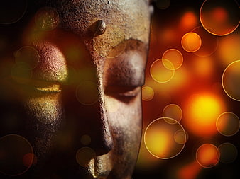 Close-up of weathered Buddha statue face with golden bokeh lights