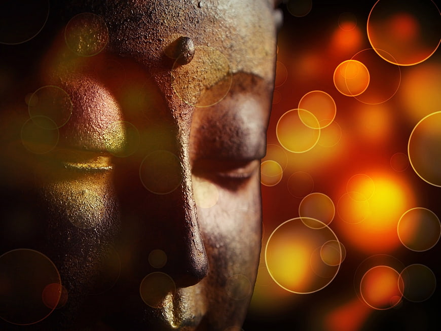 Close-up of weathered Buddha statue face with golden bokeh lights