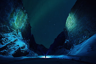Silhouette of Person with Flashlight in Snowy Canyon Under Aurora Borealis