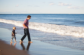Father and son walking barefoot on sandy beach