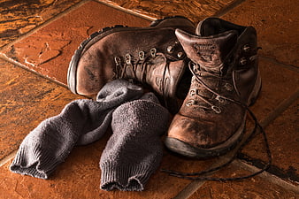 Worn brown leather hiking boots and gray wool socks on terracotta tiles