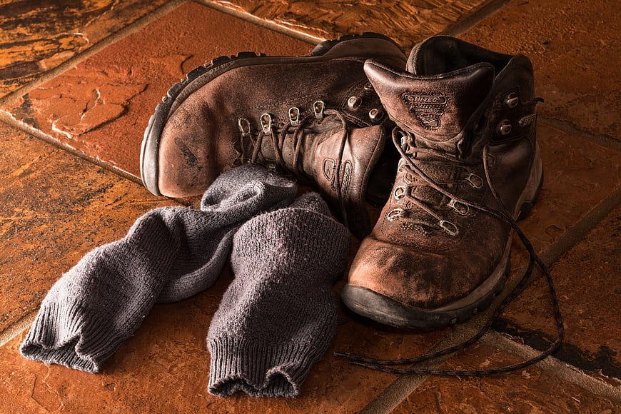 Worn brown leather hiking boots and gray wool socks on terracotta tiles