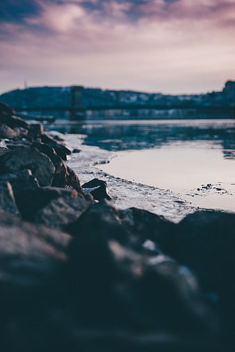 Moody Coastal Rocks at Dusk with Blurred City Skyline