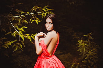 Young woman in red dress posing in dark forest