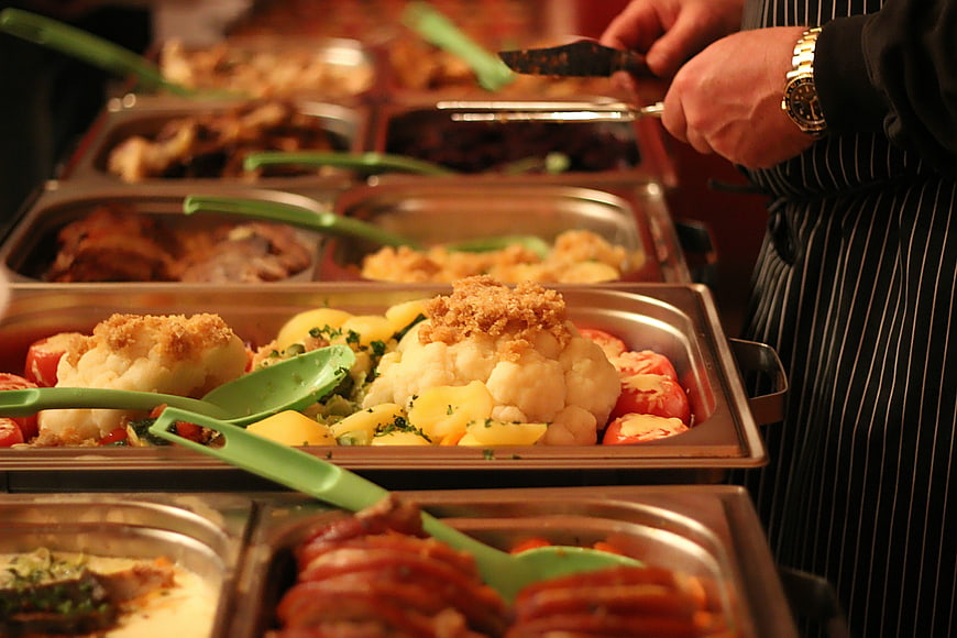 Chef serving hot buffet food in stainless steel trays
