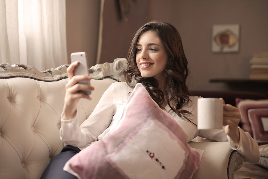 Smiling woman relaxing on sofa with smartphone and coffee