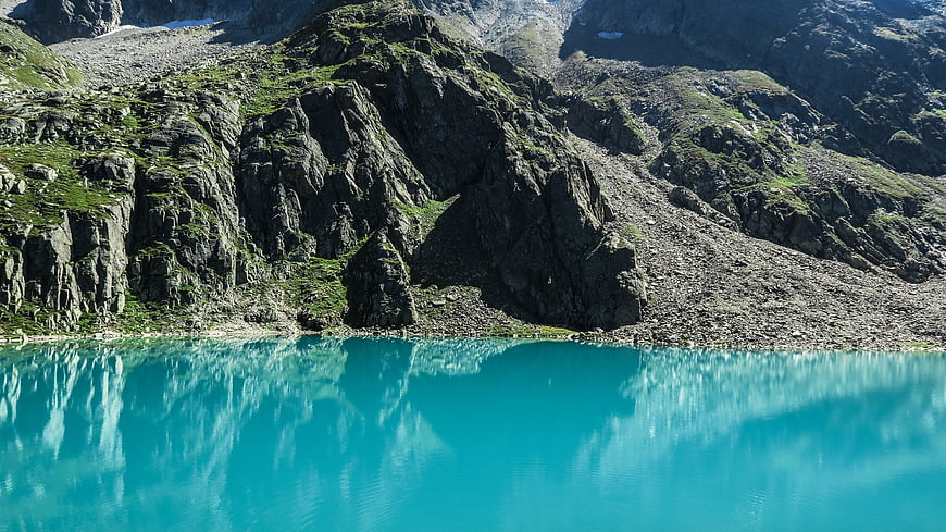 Turquoise alpine lake reflecting rugged mountain cliffs