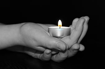 Child's hands holding a lit tea light candle in darkness