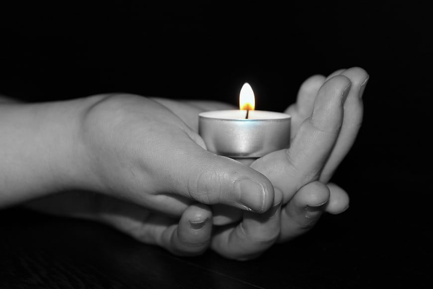 Child's hands holding a lit tea light candle in darkness