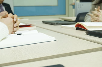 Close-up of hands clasped on desk with open notebook and laptop
