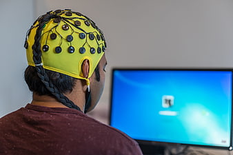 Person Wearing Yellow EEG Headset Facing Computer Monitor