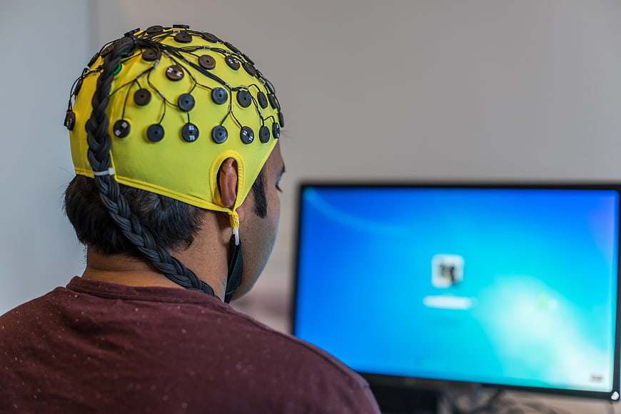 Person Wearing Yellow EEG Headset Facing Computer Monitor