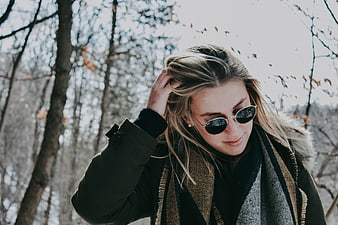 Woman in winter coat and sunglasses adjusting hair in autumn forest