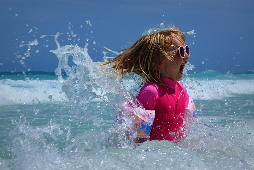 Happy child playing in ocean waves with pink swimwear