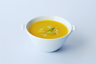White Bowl Of Yellow Pumpkin Soup With Green Herb Garnish