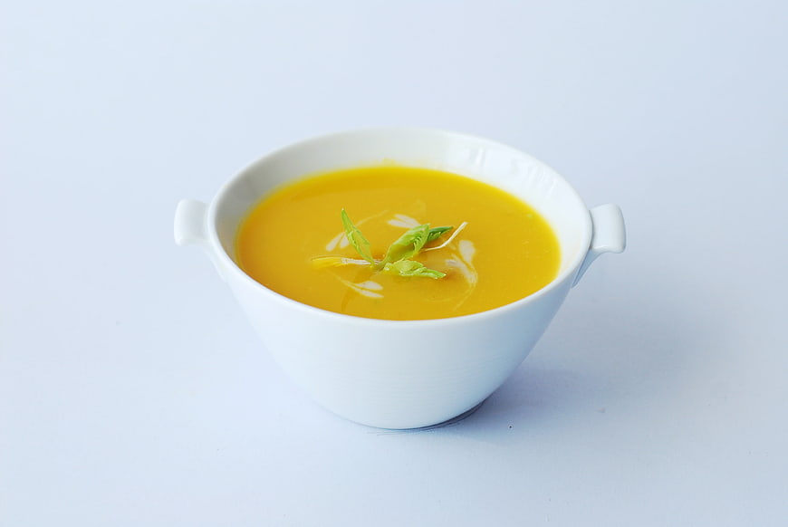 White Bowl Of Yellow Pumpkin Soup With Green Herb Garnish