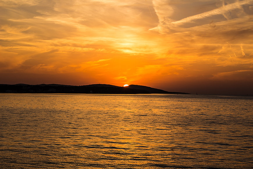 Golden sunset over calm ocean with silhouetted island hills