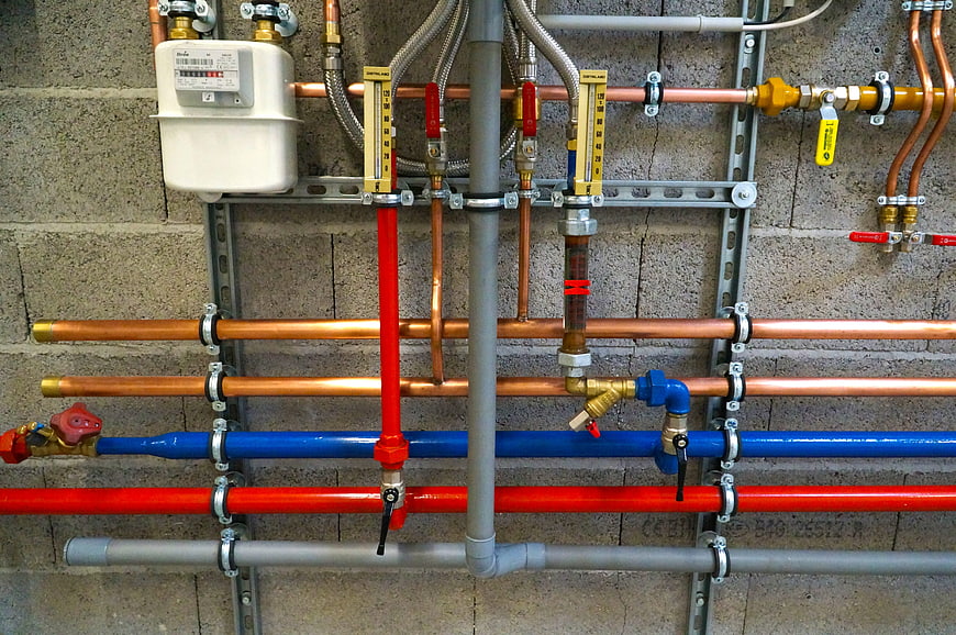 Organized copper and plastic plumbing pipes on concrete wall