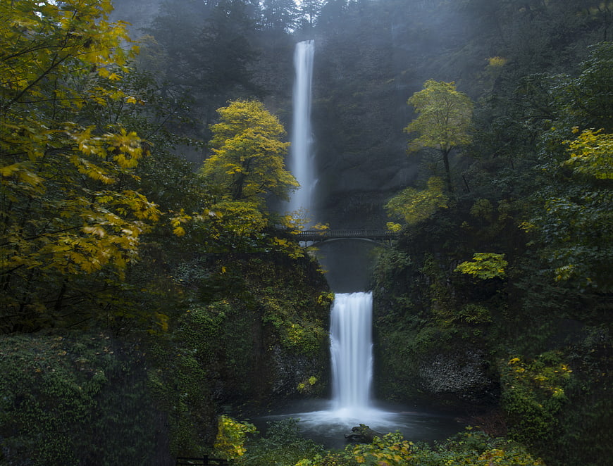 Misty waterfall cascading through lush autumn forest with bridge