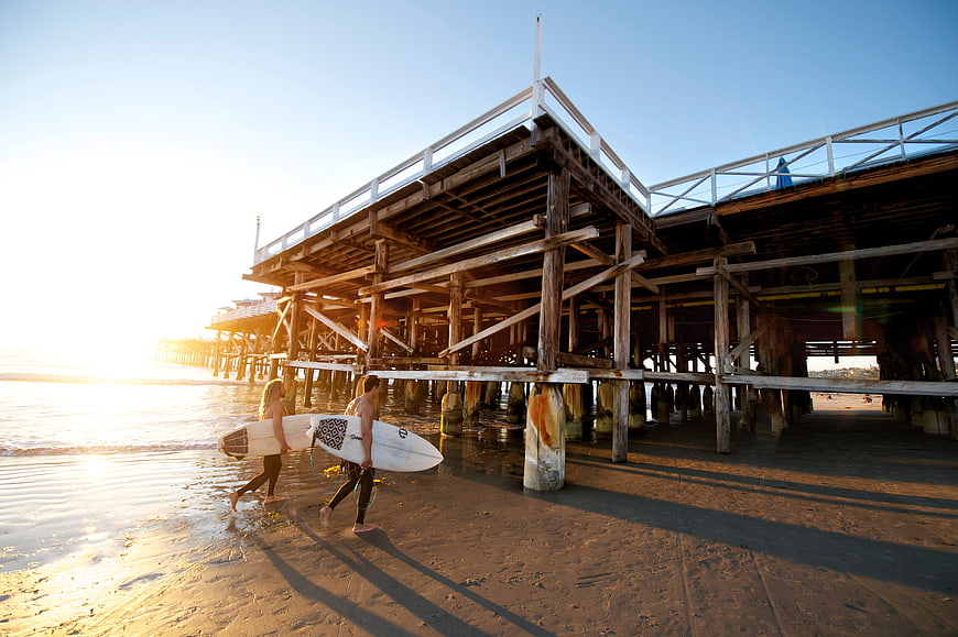 Surfers walking under pier at sunset