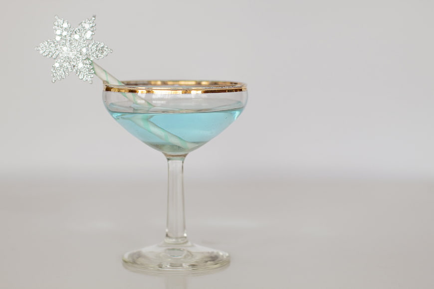 Blue Holiday Cocktail with Snowflake Garnish in Gold-Rimmed Glass