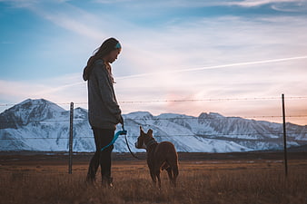 Young Woman Walking Dog in Mountain Field at Sunset