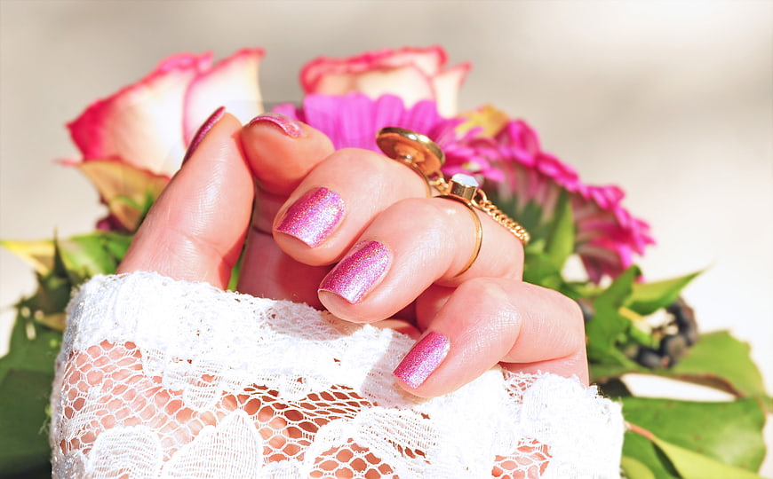 Close-up of pink glitter manicure with wedding bouquet