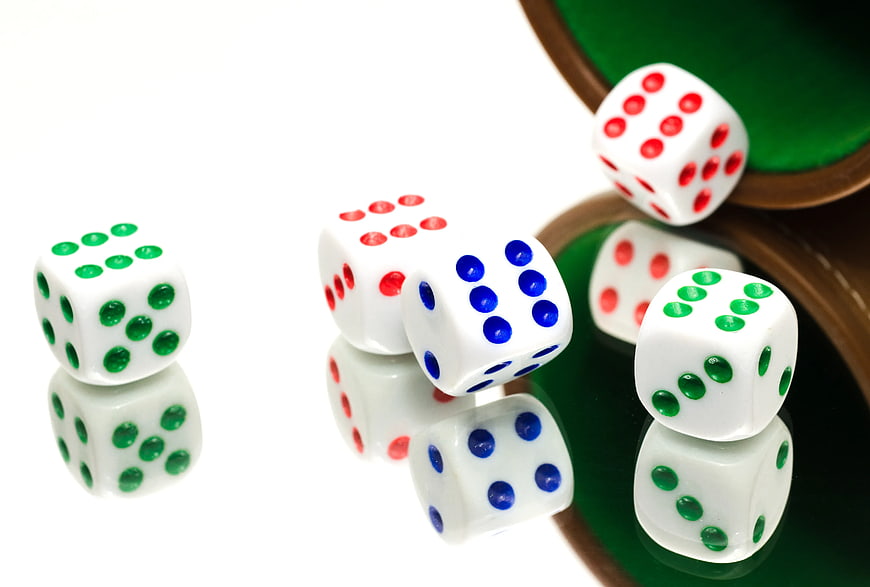 Colorful dice spilling from a cup on a reflective surface