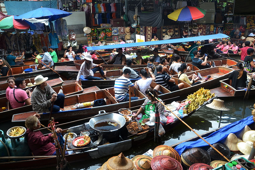 Crowded Thai floating market with boats, food vendors, and tourists