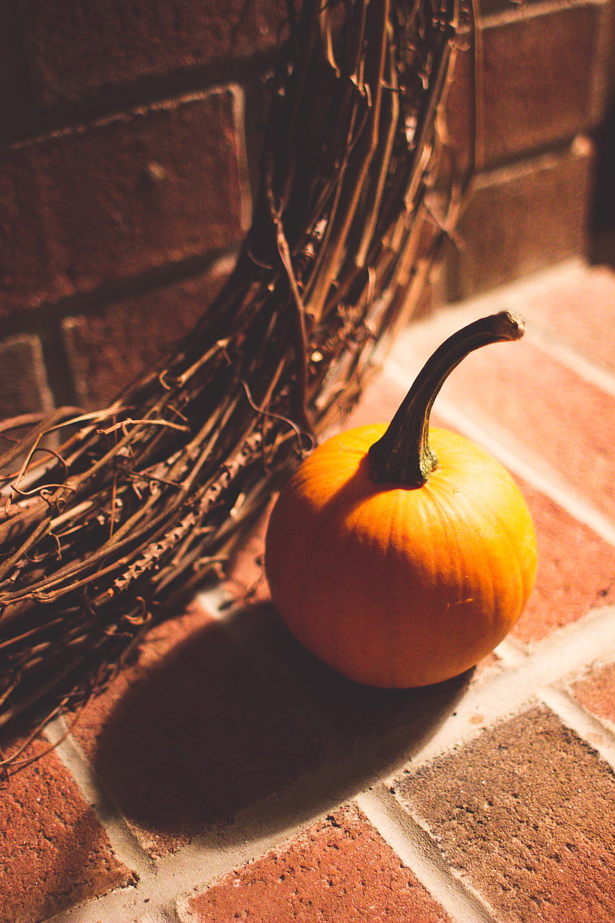 Small orange pumpkin on brick step with autumn wreath