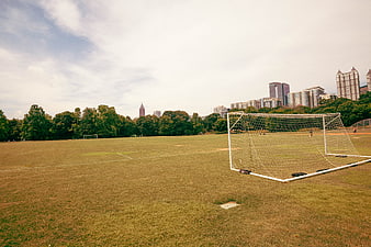 Empty Soccer Field with Goal Net and City Skyline Background