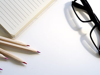 Minimalist workspace with notebook, pencils, and glasses on white desk