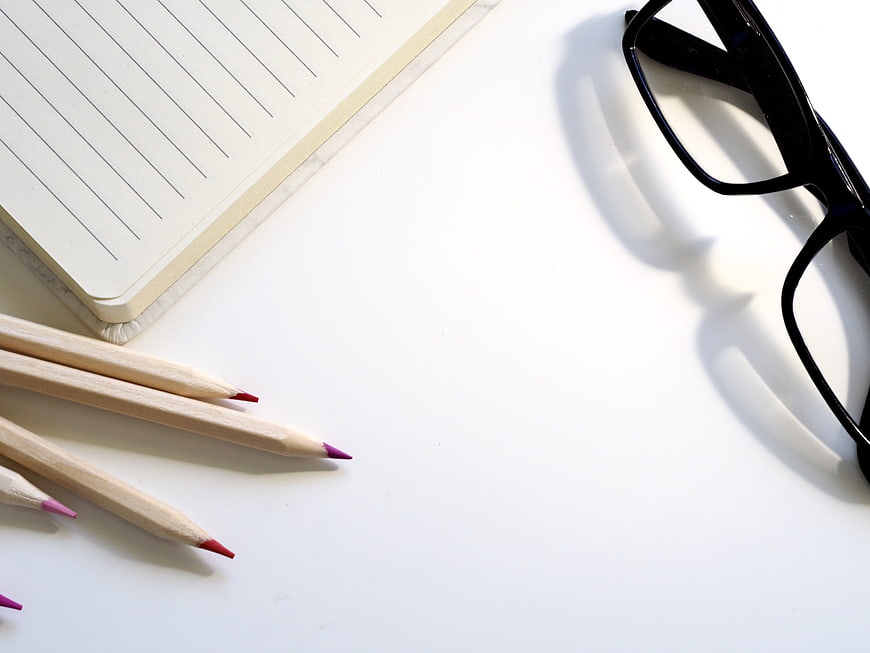 Minimalist workspace with notebook, pencils, and glasses on white desk