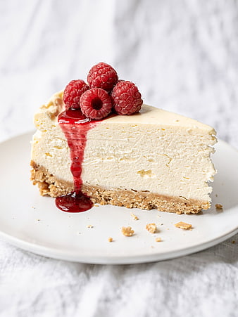 Slice of creamy cheesecake with fresh raspberries and berry sauce