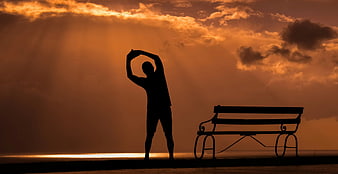 Silhouette of man stretching at sunset by the sea