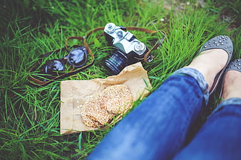Vintage camera, sunglasses, and cookies on grass with woman's legs