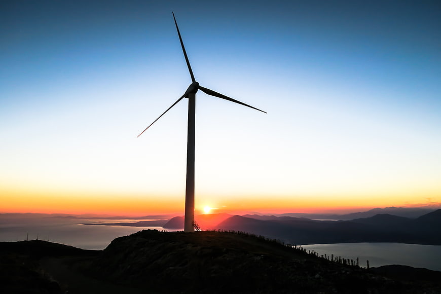Silhouette of wind turbine on mountain ridge at sunset