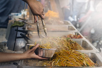 Street food vendor serving steaming noodles from buffet tray