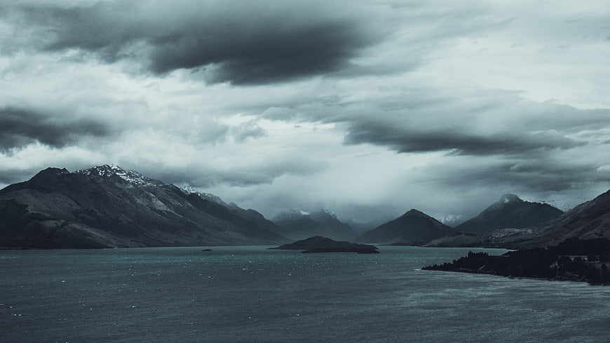 Dramatic moody landscape of mountains and lake under stormy clouds